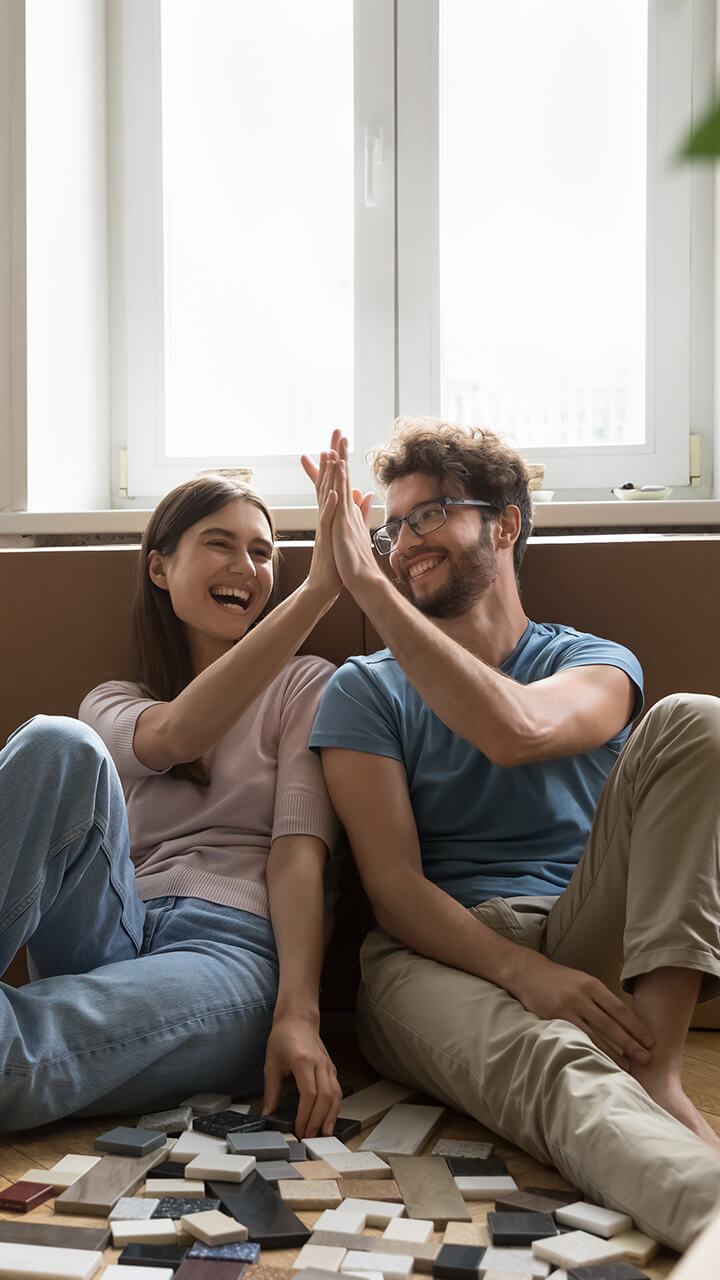 Lachendes Paar sitzt zwischen Umzugskartons und plant Bodenbelag.