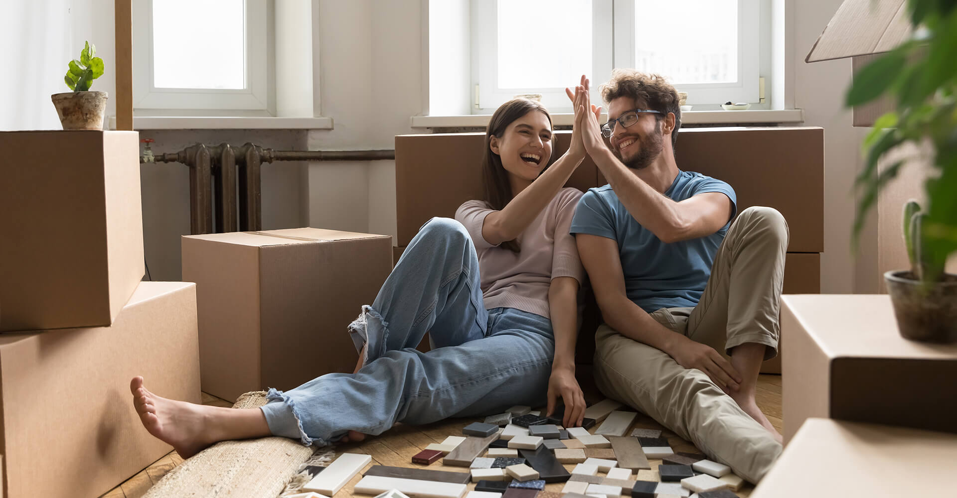 Lachendes Paar sitzt zwischen Umzugskartons und plant Bodenbelag.