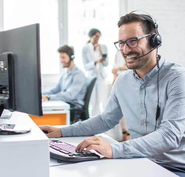 Lachende Person sitzt mit Headset vor einem Computer
